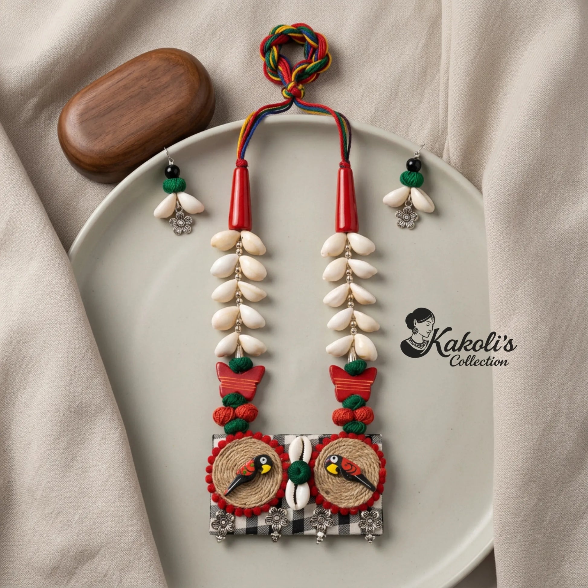 Bohemian Parrot and Cowrie Shell Handmade Fabric Necklace Set on a beige surface, featuring the 'Kakoli's Collection' logo.