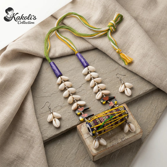 Tribal Rhythms Dhol and Cowrie Handmade Fabric Necklace Set is placed  on a textured surface with 'Kakoli's Collection' branding.