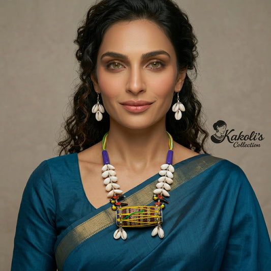 Woman wearing a blue saree with a Tribal Rhythms Dhol and Cowrie Handmade Fabric Necklace Set, with 'Kakoli's Collection' logo.
